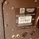 Detail zadní strany basového reproduktoru s černým povrchem a dvěma vstupními konektory. Na bílém štítku je logo Ampeg a nápisy: MODEL: SVT410HE, IMP…