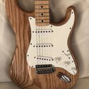 Elektrická kytara s přírodním dřevěným povrchem těla a hmatníkem z jasného dřeva. Má bílý pickguard, tři bílé snímače typu single-coil a chromovaný m…