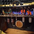 Fotografie zachycuje vnitřek kytarového komba s otevřeným chassis. Vevnitř jsou vidět elektronické součástky, zapojení kabelů a čtyři elektronky. Na…