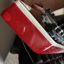 Detailní pohled na hranu červeného nástroje s bílým lemem. Povrch lakování je v pravé dolní části odloupený a vykazuje známky opotřebení. Na fotce ne…