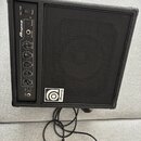 Černý basový kombozesilovač s texturovaným povrchem a černou přední síťovkou. Na ovládacím panelu jsou nápisy BA-108, Ampeg, Power, Phones, AUX Input…