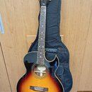 Akustická kytara s cutawayem v barevném přechodu od žluté přes oranžovou k hnědé. Na hlavě je bílý nápis Epiphone a logo v podobě písmena E. Uvnitř o…