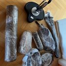 Sada komponentů elektronické bicí soupravy zabalených v průhledné potravinářské fólii. Soubor obsahuje černý stojan s kovovými trubkami, několik čern…