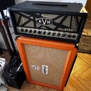 Černý kytarový zesilovač s logem EVH a označením 5150 III TUBE EL34. Pod ním stojí oranžový kytarový kombozesilovač s logem ORANGE. Oba přístroje jso…
