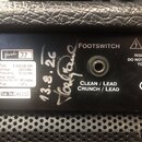 Detail zadní strany černého kytarového komba s texturovaným povrchem. Na štítku je uvedeno Grade 32, Type E 320 322 325, Voltage 230 Volts ~, Frequen…