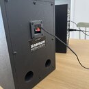 Zadní strana černého studiového monitoru s dvěma bassreflexními otvory. Na přístroji je viditelný červený vypínač a štítek s nápisy LEFT SPEAKER, SAM…