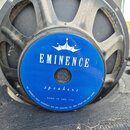 Fotografie znázorňuje reproduktor s černým kovovým rámem. Uprostřed je modrý štít s bílým nápisem EMINENCE, pod ním je symbol koruny a slovo speakers…