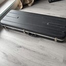 Černý tvrdý kufýr na hudební nástroj s kovými zapínacími prvky a úchytem. Na přední straně je umístěno malé stříbrné logo s nečitelným nápisem. Povrc…