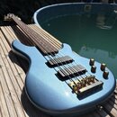 Modrá elektrická basová kytara s kovovými zlatými prvky. Nástroj má dva černá humbuckery, čtyři zlaté potenciometry a zlatý most. Na krku jsou vidět…