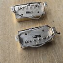 Dvě elektrické snímače typu humbucker se zlatým krytem, položené na dřevěném povrchu. Snímače jsou zobrazeny z rubové strany, kde je vidět kovová zák…