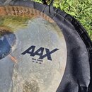 Kovový činel v žlutozlaté barvě s viditelnou strukturou povrchu. Na povrchu je černý nápis AAX a pod ním text Thin Crash 18"/45 cm. Činel leží na čer…