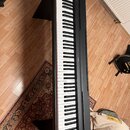 Černý digitální piano s klávesnicí a dvěma bočními podstavy. Na horním panelu je vpravo viditelné logo YAMAHA. Povrch nástroje a klávesy vypadají čis…