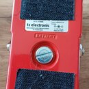 Zadní strana červeného efekt pedálu z kovu. Uprostřed je bílý štítek s nápisy „tc electronic“, „DESIGNED AND ENGINEERED IN DENMARK“, „8 V DC 100 mA M…