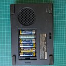 Zadní strana černého elektronického zařízení s mřížkou reproduktoru. V otevřeném prostoru pro baterie je umístěno šest AA článků značek ACTIV ENERGY,…