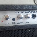 Kytarový kombozesilovač s černým texturovaným povrchem a stříbrným ovládacím panelem. Na panelu je nápis GUITAR AMPLIFIER GL-10 a ovládací prvky s po…