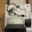 Sada bezdrátového mikrofonu v bílém polystyrenovémI balení. Obsahuje černý přijímač s nápisy XS WIRELESS 1 SENNHEISER, černý vysílač s logem Sennheis…