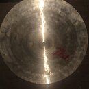 Kruhový kovový činel zlatavé barvy s viditelným broušením povrchu. Na pravé straně je červený nápis „paiste pst I“. Povrch vykazuje známky opotřebení…