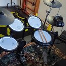 Elektronická bicí souprava značky Roland s bílými padovými plochami a černými činely. Na padech jsou viditelné nápisy Roland a V-Drums. Součástí je č…