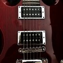 Detail elektrické kytary v tmavě červené barvě s viditnou strukturou dřeva. Nástroj má dva humbuckery s chromovanými rámečky a Tune-o-matic můstek s…