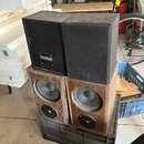 Čtyři reproduktory naskládané na sebe v plastovém přepravním boxu. Horní dva jsou černé, pravý vykazuje v horní části odřápání povrchu. Spodní dva js…