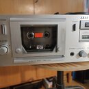 Stříbrný kazetový přehrávač značky AKAI s nápisem STEREO CASSETTE. Na předním panelu jsou tlačítka PAUSE a REC, nápisy POWER, EJECT, TAPE COUNTER, RE…