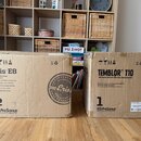 Dvě hnědé kartonové krabice stojící vedle sebe na dřevěné podlaze. Levá krabice nese nápisy „Eris E8“, „High-Definition Active Studio Monitor“ a logo…