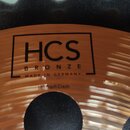 Detailní záběr na bronzový činel s koncentrickými rýhami. Na povrchu je černý nápis v rámečku „HCS BRONZE MADE IN GERMANY“ a pod ním text „18" Trash…