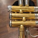 Detailní pohled na mosazné ventily trubky se stříbrnými prvky. Na prostředním ventilu je svisle vyražen nápis MADE IN JAPAN. Povrch nástroje vykazuje…