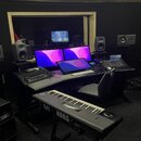 Fotografie zachycuje hudební studio s černým pracovním stolem a vybavením. V popředí je černý klávesový syntezátor s bílými klávesami a nápisem M1 KO…