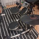 Elektronická bicí souprava s černými pady a černými činelyy na chromovaném stojanu. Na padesátých padech a na rámu je viditelný nápis LABROBRO. Součá…