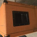Kytarový kombozesilovač nebo box s oranžovým texturovaným povrchem a černými plastovými rohy. Na boku je umístěn čtvercový otvor s černým rámečkem a…