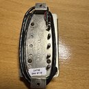 Fotografie znázorňuje spodní stranu elektrického snímače s kovovým krytem stříbrné barvy. Na spodní části je vyražen nápis „Seymour Duncan“ a pod ním…