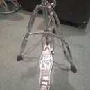 Chromovaný kovový stojan s pedálem, pravděpodobně hi-hat. Na pedálu je viditelné logo TAMA a nápis THE LEGEND IN INNOVATION. Povrch pedálu vykazuje z…