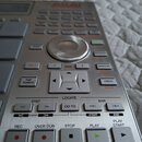 Detailní pohled na ovládací panel stříbřitého sampleru značky AKAI. Jsou vidět různé ovládací tlačítka s nápisy jako REC, OVER DUB, STOP, PLAY, PLAY…