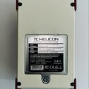 Zadní strana bílého efektového pedálu s červenými ochrannými rohy. Na stříbrném štítku je uveden název TC HELICON a nápis DESIGNED AND ENGINEERED IN…