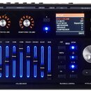 Černý elektronický perkusní modul s modrým podsvícením faderů a ovládacích prvků. V horní části jsou dva otočné ovladače s nápisy MASTER VOLUME a HEA…
