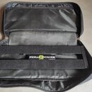 Černý pedalboard s kovovou konstrukcí a černým povrchem, umístěný v otevřeném černé transportním pouzdře. Uprostřed je viditelné bílo-zelené logo s n…