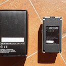 Na fotografii je černá krabice a spodní strana efektového pedálu v bílém kovovém šasi. Na krabici je nápis USE BOSS PSA ADAPTOR ONLY (DC 9V), logo CE…