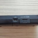 Černý elektronický přístroj s USB portem a slotem pro paměťovou kartu. Na horní hraně jsou bílé nápisy USB, micro SD a PUSH EJECT. Vpravo je umístěn…