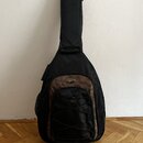 Černý polstvuovaný obal na kytaru s hnědými prvky. V horní části hnědého panelu je umístěno oválné logo, které je nečitelné. Obal má v přední části k…