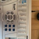 Detailní pohled na ovládací panel stříbřitého klávesového nástroje. Na povrchu je nápis Fox Instruments a seznam 128 rytmů pod nadpisem RHYTHM. Jsou…