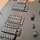 Černá elektrická kytara s tmavým hmatníkem. Na krku snímače je nápis seymour Duncan. Nástroj je vybaven Floyd Rose stylem mostu a třemi ovládacími kn…