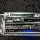 Stříbrný rackový systém s černými vložkami, který obsahuje několik zařízení a kabeláže. V horní části je panel s digitálním displejem zobrazujícím če…