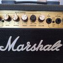 Detail kytarového komba se zlatým ovládacím panelem a černou textilní maskou. Na masce je bílé plastové logo Marshall. Panel obsahuje řadu otočných k…