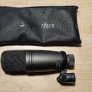 Černý mikrofon s kovovou síťkou a držákem, umístěný na světlém dřevěném povrchu. Na těle mikrofonu je viditelný nápis „CHINA“ a značka „CE“. Vedle mi…