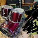 Vícedílná bicí souprava v tmavě červené barvě s kovovým kováním. Na basovém bubnu a tom-tamech jsou viditelné nápisy „YAMAHA“. Povrchy nástrojů vykaz…