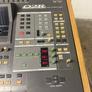 Šedá digitální mixovací konzole s nápisem O2R DIGITAL RECORDING CONSOLE. Panel obsahuje řadu tlačítek, posuvníků a červené digitální displeje s hodno…