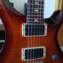 Elektrická kytara s hnědým lakovaným povrchem s viditelnou strukturou dřeva. Nástroj má dva snímače typu humbucker s bílými rámečky, na kterých je uv…