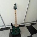 Elektrická kytara s tmavě zeleným průsvitným lakem a viditnou strukturou dřeva na těle. Na hlavě hnedníku je bílý nápis Ibanez. Nástroj má světlý hma…