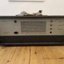 Zadní strana šedého elektronického zařízení v černém rámu. Na panelu jsou nápisy „Netzsicherung 1,6A“, „Netzanschluß Wechselstrom 220V“ a vpravo sekc…